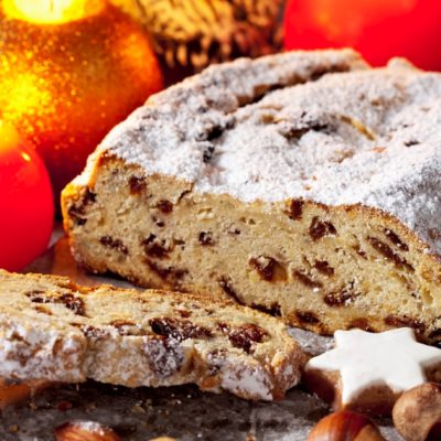 Dredner Christstollen mit Rosinen, Messer,  Holzbrett, Weihnachtsgebäck, Weihnachtsdeko, Zimtstern, Nüsse, Zimtstangen,Tannenzweig, rote, goldene, Kerzen, Stern, Nikolaus, Weihnachtsgeschenk,  Weihnachten, xmas, x-mas, grauer Holzuntergrund, Holztisch, Studio